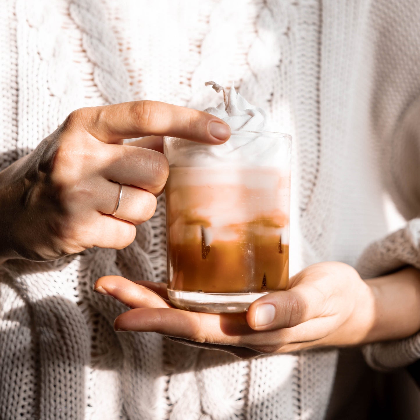 Person holding a glass of iced coffee with a white sweater