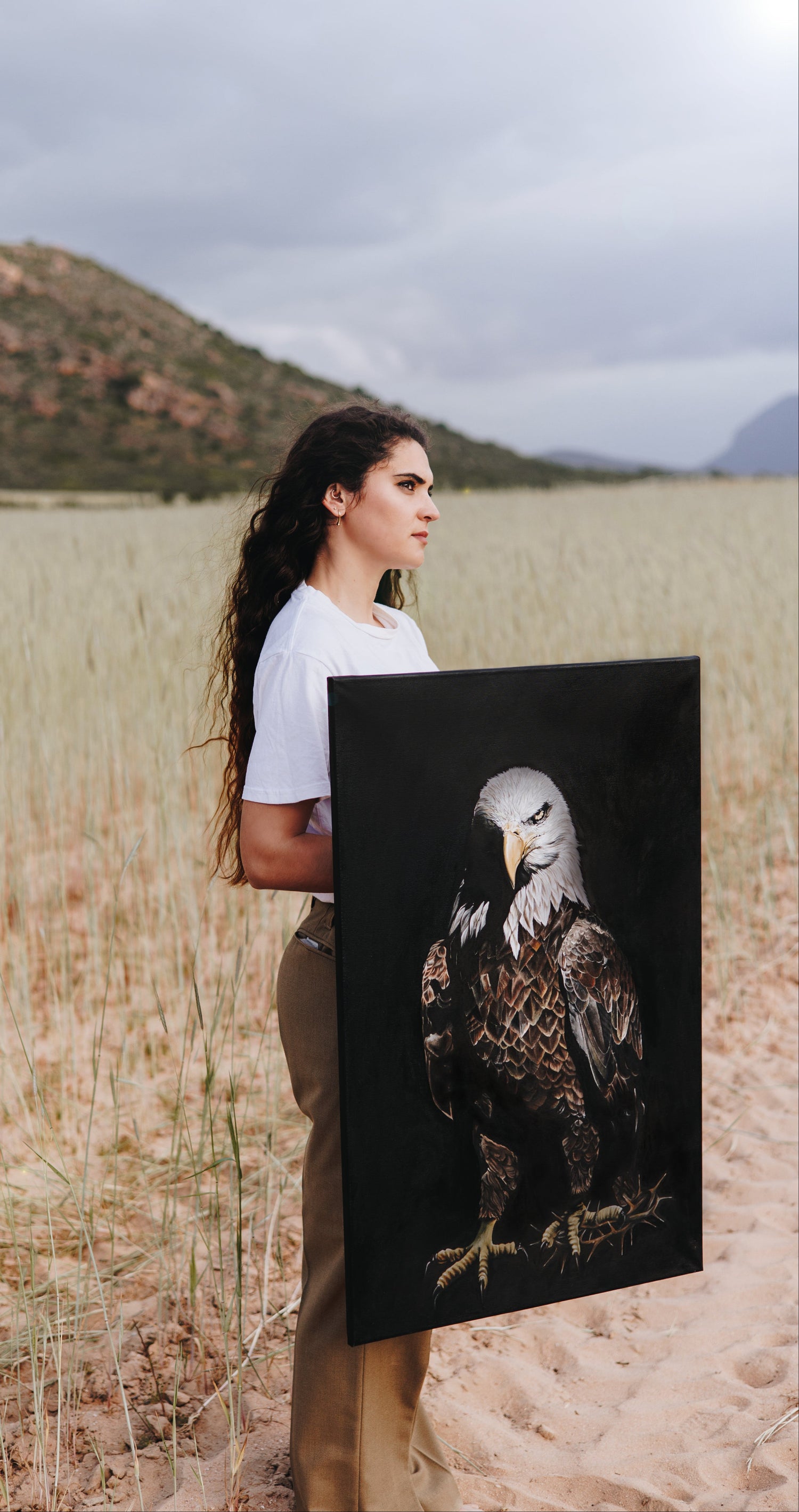 Woman holding a painting of an eagle in a natural landscape