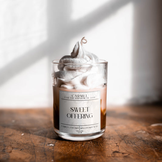 Candle labeled 'Sweet Offering' on a wooden surface with a blurred background